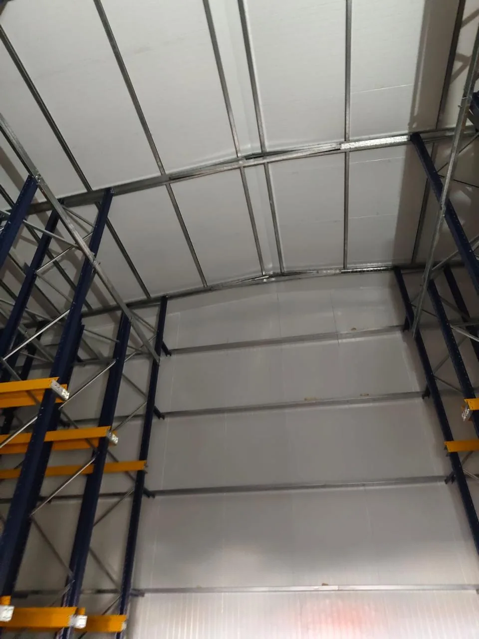 Estanterías de paletización de gran altura y un operario en un elevador de tijera bajo la cubierta de la bodega
